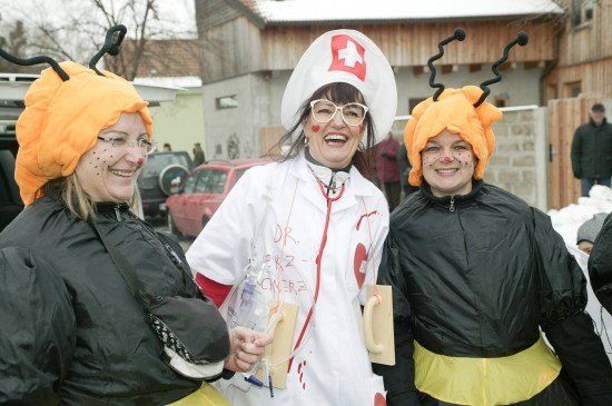 Drei Frauen in Kostümen, zwei in Bienenkostümen und eine in einem Arztuniform, stehen zusammen draußen.