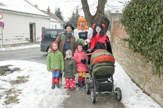 Eine Familie in Kostümen steht auf einer verschneiten Straße mit einem Kinderwagen und zwei Erwachsenen vor ihnen.