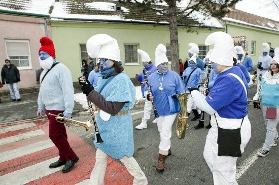 Eine Gruppe von Menschen in blauen und weißen Kostümen mit blauen Gesichtern und weißen Hüten zieht in einem Umzug und spielt Musikinstrumente.