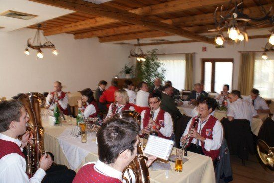 Eine Gruppe von Musikern in roten Westen spielt Instrumente bei einem Bankett in einem holzbalkengedeckten Raum.