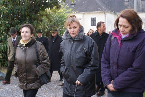 Eine Gruppe von Menschen, darunter Frauen in Wintermänteln, geht vor einem Gebäude. Die Frau in der Mitte hält eine Leine.