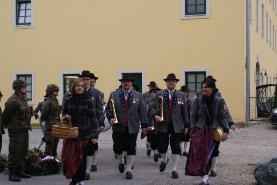 Eine Gruppe von Menschen in traditionellen Uniformen und mit Musikinstrumenten in der Hand geht in einer Reihe vor einem gelben Gebäude.