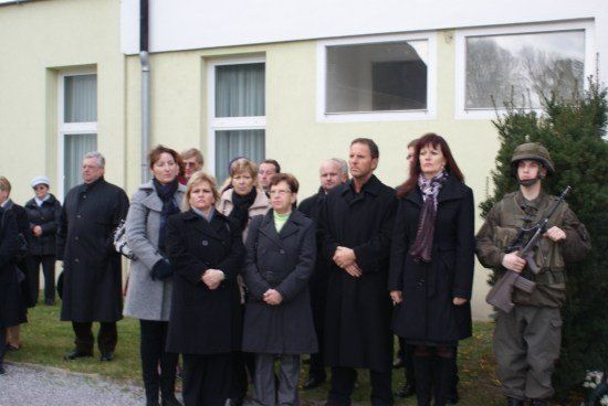 Eine Gruppe von Menschen in Wintermänteln steht vor einem Gebäude, wobei eine Person in Uniform eine Waffe hält.