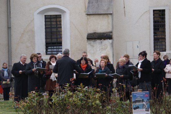 Ein Chor von Menschen in Winterkleidung steht vor einem Gebäude und hält Notenblätter in den Händen.