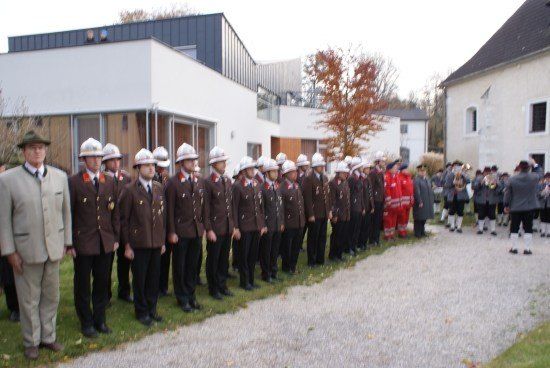 Eine Gruppe von Feuerwehrleuten in Uniform steht in einer Reihe vor einem Gebäude mit einem Baum im Hintergrund.
