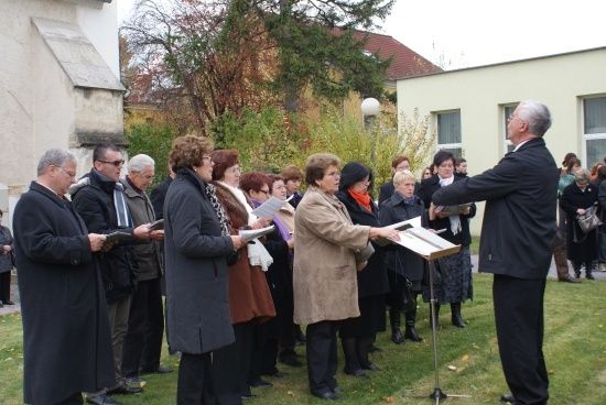 Eine Gruppe von Menschen in Winterkleidung steht in einer Reihe, hält Bücher und singt vor einem Gebäude.