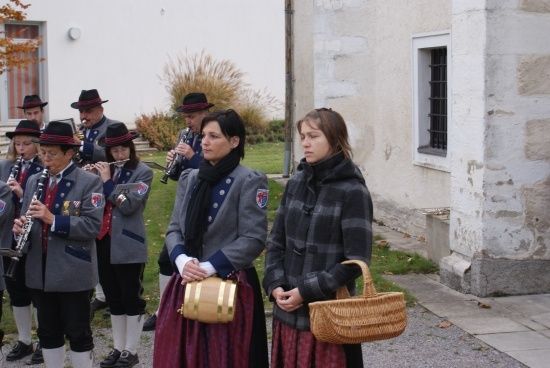 Eine Gruppe von Musikern in traditioneller Kleidung steht vor einem Gebäude, wobei eine Frau einen Korb hält.