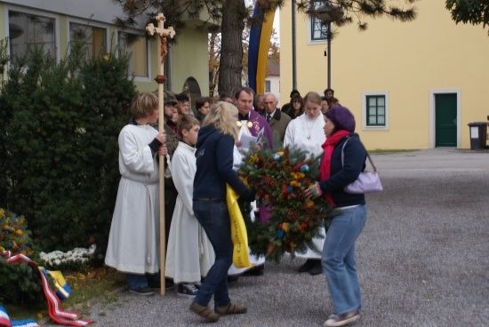 Eine Gruppe von Menschen, einschließlich eines Priesters, versammelt sich um einen Kranz vor einer Kirche.