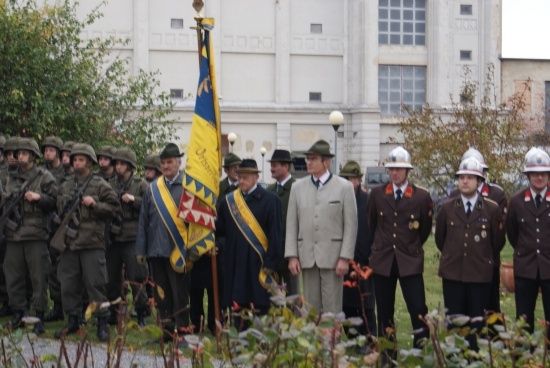 Eine Gruppe von Männern in Militäruniformen und Mützen steht vor einem Gebäude, einige halten eine Flagge und andere tragen Medaillen.
