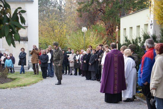 Eine Gruppe von Menschen, darunter ein Soldat in Uniform, steht in einer Reihe vor einer Kirche, möglicherweise bei einer Zeremonie.