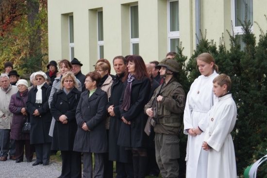 Eine Gruppe von Menschen in Winterkleidung steht vor einem Gebäude, einige in weißen Gewändern, wahrscheinlich bei einer Zeremonie.