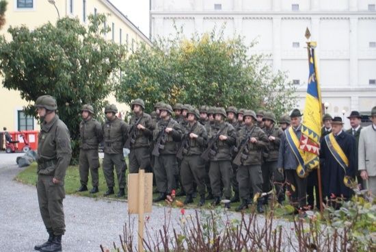 Eine Gruppe von Soldaten in Uniform steht in Formation vor einem Gebäude mit einer Fahne auf einem Pfahl.