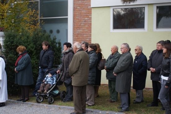 Eine Gruppe von Menschen in Winterkleidung steht in einer Reihe vor einem Gebäude, einige halten sich an den Händen und andere haben Kinder bei sich.
