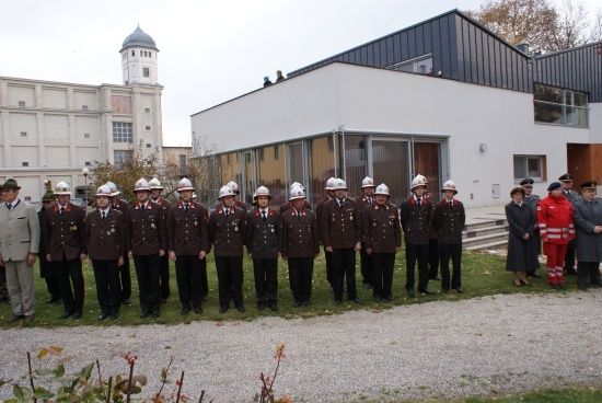 Eine Gruppe von Feuerwehrleuten in Uniform steht vor einem modernen Gebäude mit Turm und großem Fenster.