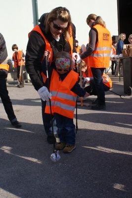 Eine Frau in einer orangefarbenen Warnweste hilft einem kleinen Kind mit einer Augenbinde, an einem sonnigen Tag mit einem Golfball zu spielen.