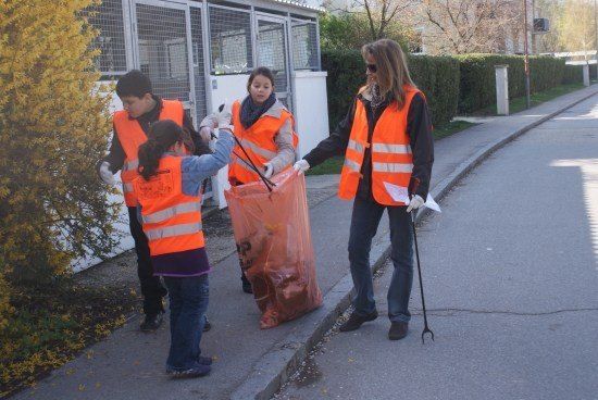 Eine Gruppe von Menschen in orangenen Westen sammelt Müll am Straßenrand.