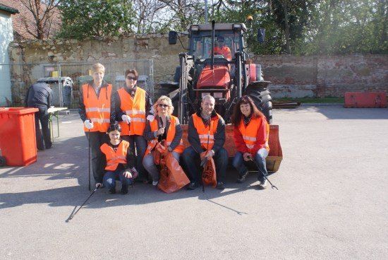 Eine Gruppe von Menschen in orangefarbenen Westen posiert für ein Foto vor einem Traktor und einer Ziegelmauer.