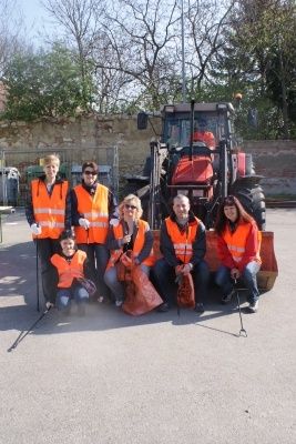 Eine Gruppe von Menschen in orangefarbenen Westen posiert für ein Foto vor einem Traktor. Sie halten Müllsäcke in den Händen und scheinen Teil einer Gemeinschaftsaktion zur Müllentsorgung zu sein.
