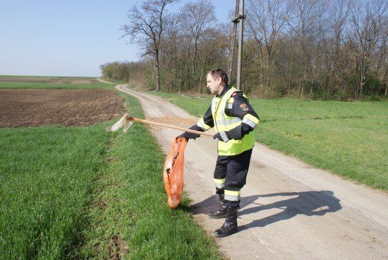 Ein Mann in einer Warnweste und Stiefeln sammelt Müll an einer unbefestigten Straße auf.