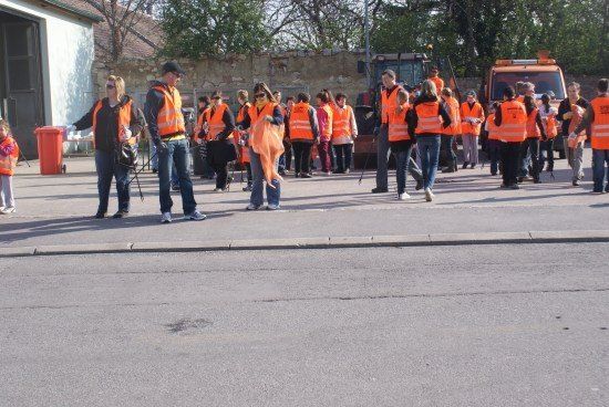 Eine Gruppe von Menschen in orangefarbenen Westen geht auf einer Straße, möglicherweise an einer Gemeindereinigungsveranstaltung teilnehmend.