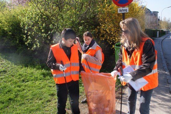 Drei Freiwillige in orange Westen sammeln Müll in einer Nachbarschaft, einer hält einen Beutel und die anderen zwei halten Stöcke.