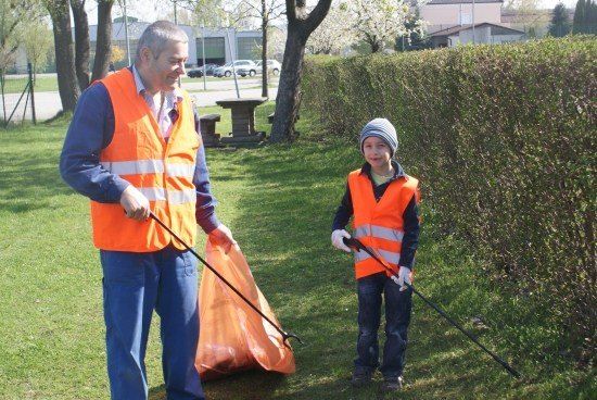 Ein Erwachsener und ein Kind in Warnwesten sammeln Müll in einem Park.