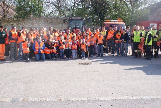 Eine Gruppe von Menschen in orangefarbenen Warnwesten posiert für ein Foto vor einer Straße mit Maschinenfahrzeugen im Hintergrund.
