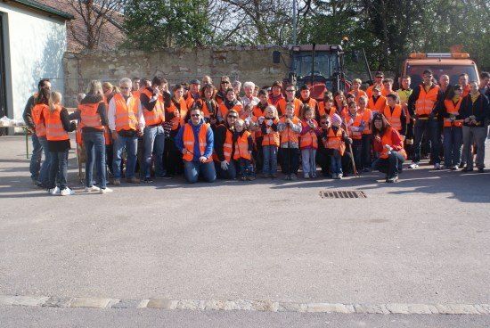 Eine Gruppe von Menschen in orangenen Westen posiert für ein Foto vor einem Gebäude mit Maschinenfahrzeugen im Hintergrund.