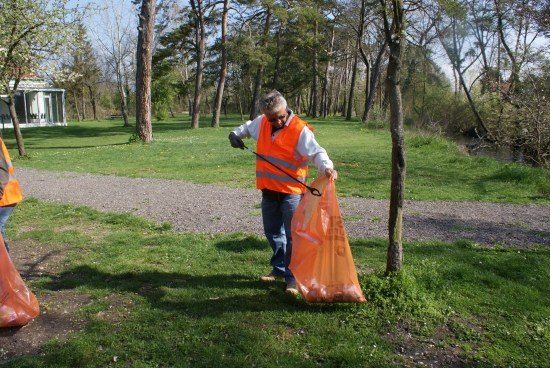 Eine Person in einem orangefarbenen Warnweste sammelt Müll in einem Park.