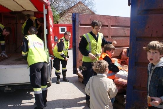 Eine Gruppe von Personen in Sicherheitswesten entlädt Gegenstände aus einem LKW. Einige Kinder beobachten.