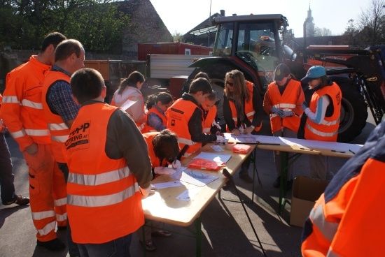 Eine Gruppe von Menschen in orangenen Sicherheitswesten arbeitet draußen an einem Projekt, mit einem Traktor im Hintergrund.