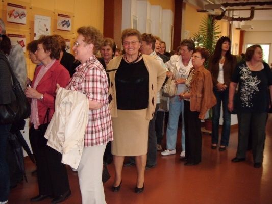 Eine Gruppe von Frauen, einige mit Brille, stehen in einem Raum mit gelben Wänden und einem braunen Boden, möglicherweise warten sie in einer Schlange.