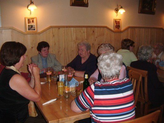 Eine Gruppe älterer Menschen sitzt um einen Holztisch in einem Restaurant, mit Getränken und Essen auf dem Tisch.