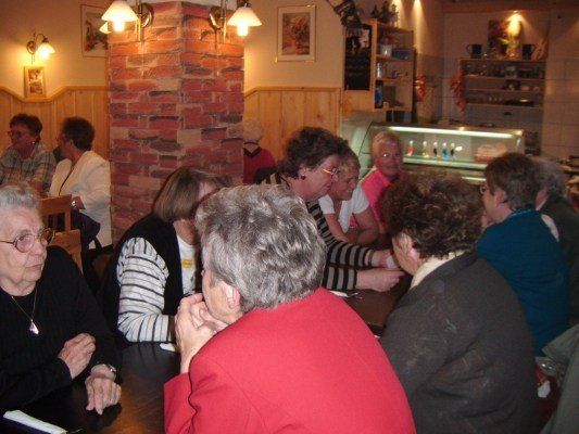 Eine Gruppe älterer Frauen sitzt in einem Restaurant um einen Tisch herum und unterhält sich. Der Raum ist warm beleuchtet mit Ziegelwänden und Holzakzenten.