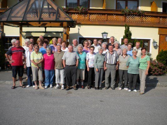 Eine Gruppe älterer Menschen steht vor einem Gebäude mit Balkon und Pavillon.