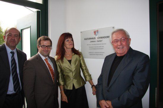 Vier Personen stehen vor einer weißen Wand mit einem Schild, auf dem 'Kulturhaus Schwäbisch Gmünd' steht. Der Mann links trägt eine gestreifte Krawatte, der Mann neben ihm trägt eine Brille und eine orangefarbene Krawatte. Die Frau in der Mitte hat rote Haare und trägt eine Halskette. Der Mann rechts lächelt.
