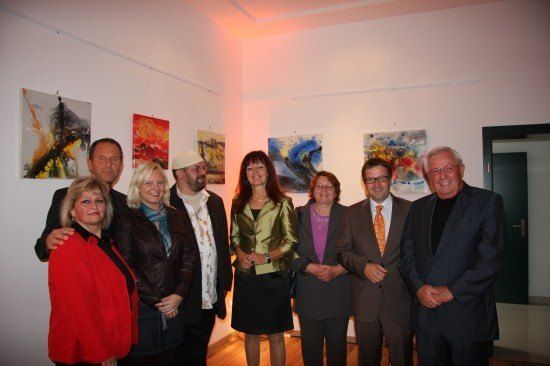 Eine Gruppe von Menschen posiert für ein Foto in einer Kunstgalerie mit verschiedenen Gemälden an der Wand.