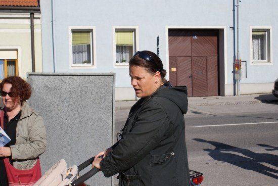 Eine Frau schiebt einen Kinderwagen die Straße entlang, während eine andere Frau ein Buch liest.