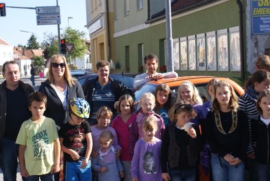 Eine Gruppe von Erwachsenen und Kindern, darunter ein Junge mit Helm, posiert für ein Foto vor einem orangefarbenen Auto.