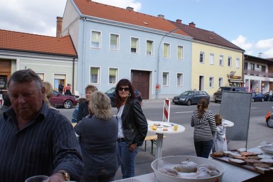 Eine Gruppe von Menschen versammelt sich um einen Tisch mit Essen auf einer Straße vor Gebäuden.