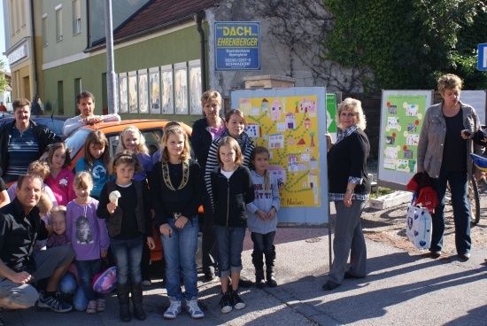 Eine Gruppe von Menschen, einschließlich Erwachsener und Kindern, posiert für ein Foto vor einem Gebäude mit einem Schild, das 'DACH' steht. Die Kinder halten Eistüten in der Hand.