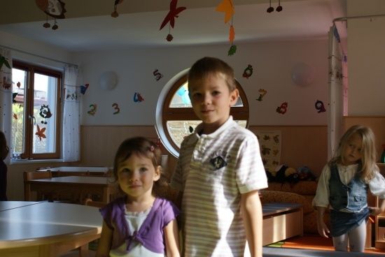 Drei Kinder stehen in einem Klassenzimmer mit einem runden Fenster und Dekorationen an der Wand.