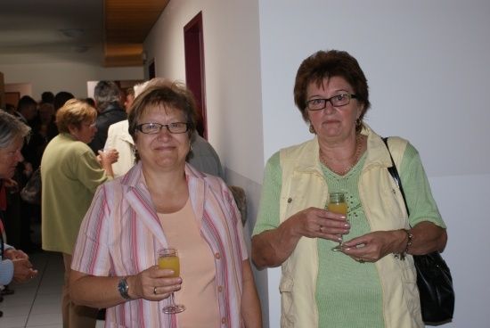 Zwei Frauen, eine mit Brille und Ring, halten Weingläser in einem überfüllten Raum.