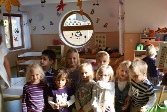 Eine Gruppe von Kindern in einem Klassenzimmer mit einem runden Fenster und dekorierten Wänden, einige lächeln und andere schauen weg.