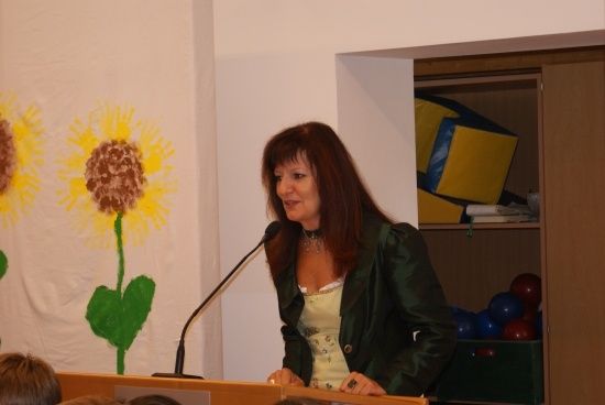 Eine Frau steht an einem Rednerpult und spricht in ein Mikrofon. Hinter ihr ist eine Wand mit einer Sonnenblumenmalerei.
