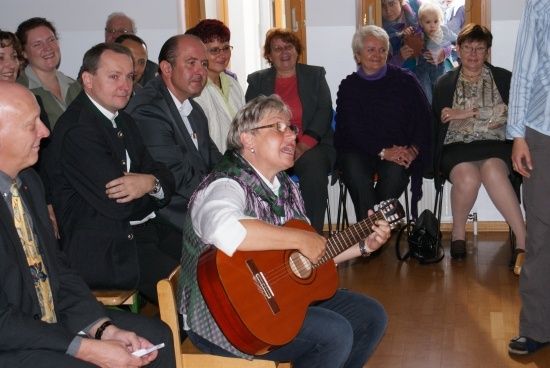 Eine Gruppe von Menschen in einem Raum, eine Frau spielt Gitarre, während andere zusehen.