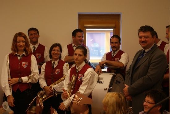 Eine Gruppe von Musikern in roten Westen, darunter eine Frau mit einem Posaune, posiert für ein Foto mit einem Schlagzeug im Vordergrund.