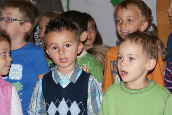 Eine Gruppe junger Kinder steht zusammen, möglicherweise in einem Klassenzimmer oder einer Schulumgebung. Sie alle schauen in die gleiche Richtung.