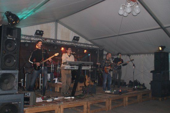 Eine Band spielt auf einer Bühne unter einem Zelt mit Lautsprechern und Beleuchtungsequipment.