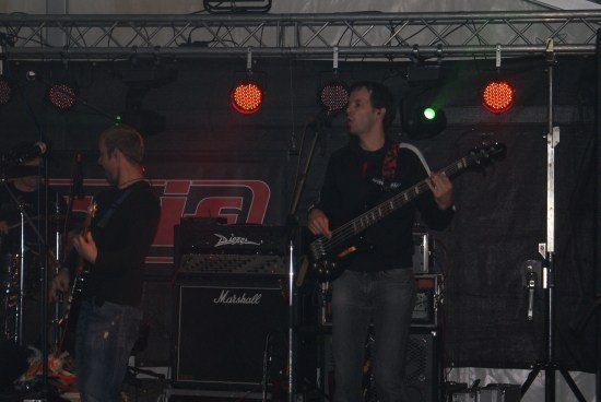 Zwei Männer auf der Bühne spielen Gitarren unter roten und grünen Bühnenlichtern. Ein Mann singt in ein Mikrofon.